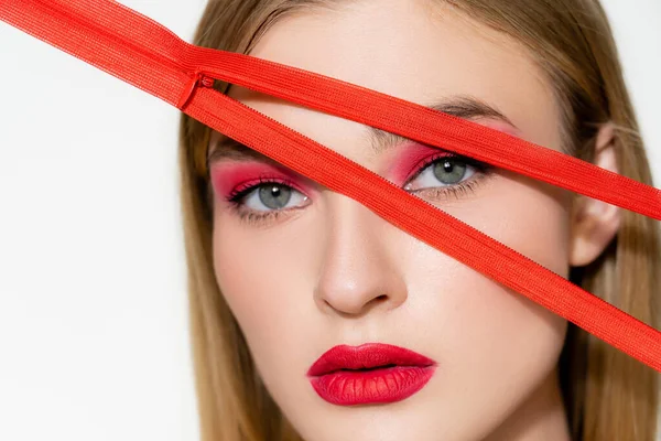 Mujer joven con labios rojos mirando a la cámara cerca de la cremallera aislada en blanco - foto de stock