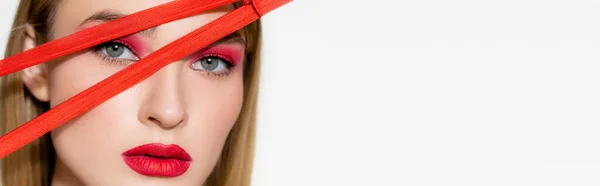 Modelo joven con sombra de ojos rojos y labios mirando a la cámara cerca de la cremallera aislada en blanco, pancarta - foto de stock