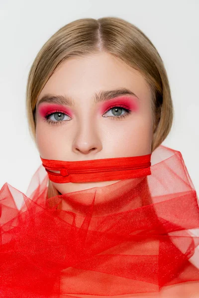 Mujer joven con cremallera roja en la boca y tela de tul aislada en gris - foto de stock