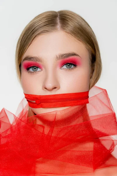 Young woman with red zipper on mouth and tulle cloth isolated on grey — стоковое фото