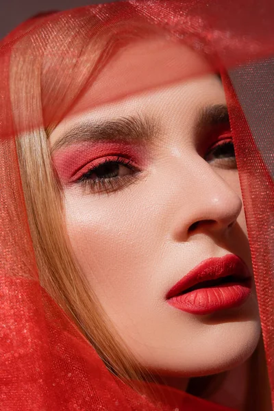 Portrait de jeune modèle aux cheveux blonds avec visage rouge regardant loin près du tissu sur fond gris — Photo de stock