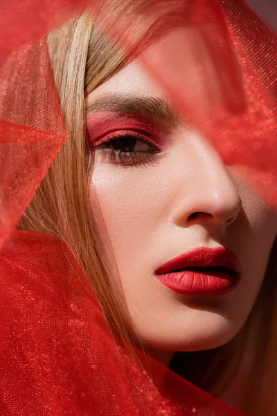 Model with red visage and obscure face looking at camera near cloth — Stock Photo