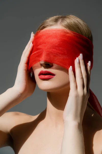 Femme aux épaules nues et aux lèvres rouges touchant le tissu sur le visage isolé sur gris — Photo de stock