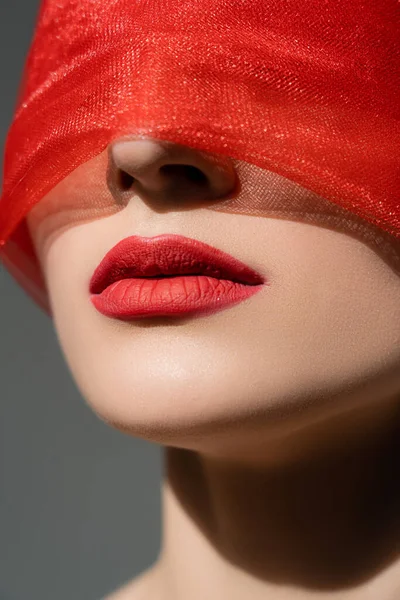 Vista de cerca de la mujer con tela roja en la cara de pie aislado en gris - foto de stock