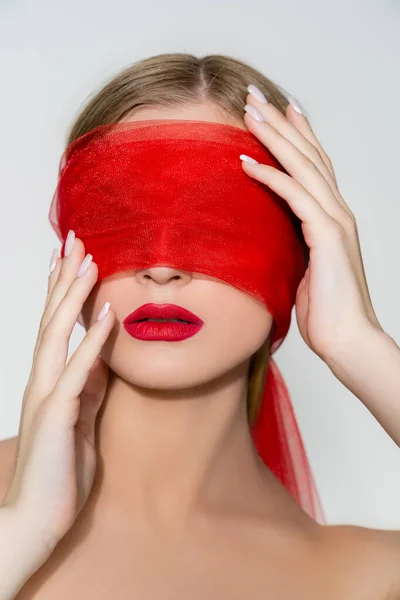 Mujer de pelo rubio con labios rojos tocando tela en la cara aislada en gris - foto de stock