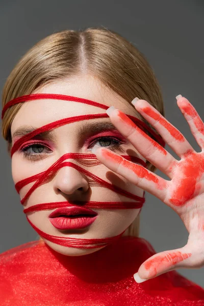 Modèle avec visage rouge, fils et peinture à la main isolés sur gris — Photo de stock