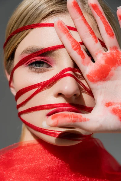 Portrait of woman with red threads on face and paint on hand isolated on grey — Stock Photo