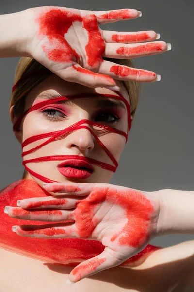 Young woman with red visage, threads and paint on hands posing isolated on grey — стоковое фото