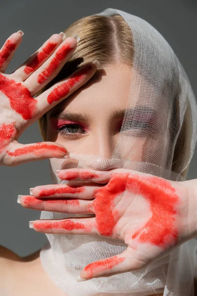 Modell mit medizinischem Verband im Gesicht und roter Farbe an den Händen isoliert auf grau — Stockfoto