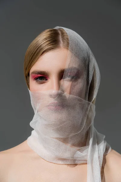 Young woman with naked shoulders and medical bandage on face looking at camera isolated on grey — стоковое фото