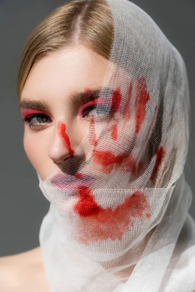 Jeune femme avec impression rouge de la main sur bandage médical sur le visage isolé sur gris — Photo de stock