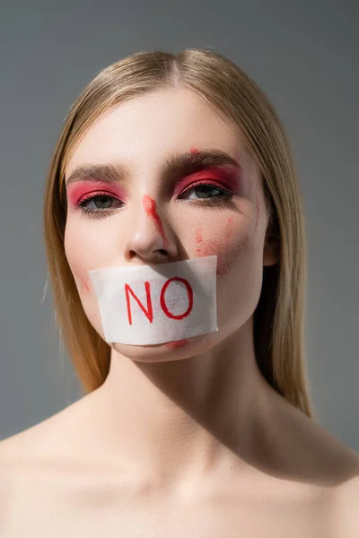 Mujer joven con maquillaje rojo y tarjeta sin letras en los labios mirando a la cámara aislada en gris - foto de stock