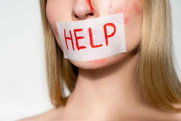 Cropped view of paper with help lettering on lips of woman with blood on face isolated on grey — Stock Photo