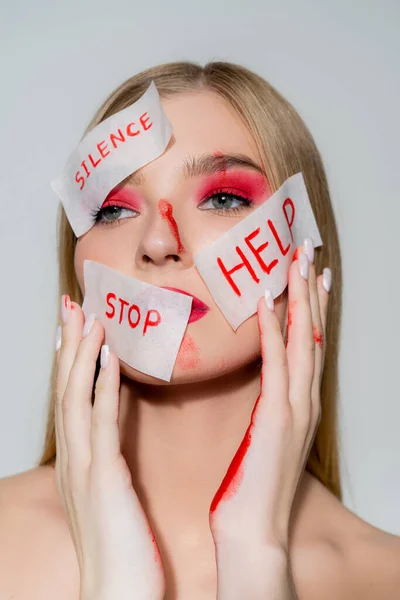 Jovem com tinta nas mãos e papéis com silêncio, parar e ajudar a lettering no rosto isolado em cinza — Fotografia de Stock