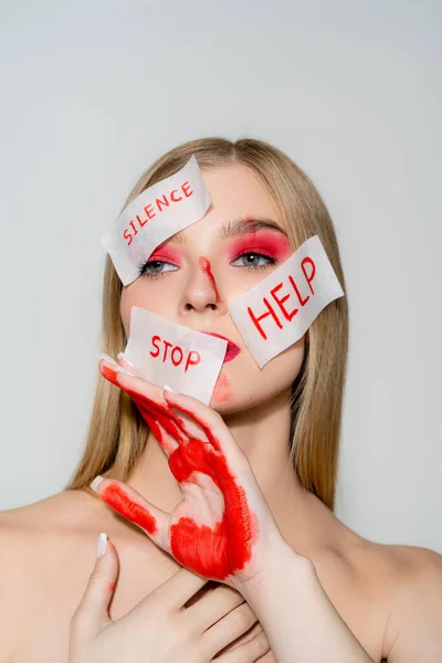 Young woman with red visage and papers with silence, stop and help lettering isolated on grey — Stock Photo