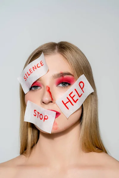 Donna con sangue e carte con silenzio, stop e aiuto lettering sul viso guardando la fotocamera isolata su grigio — Foto stock