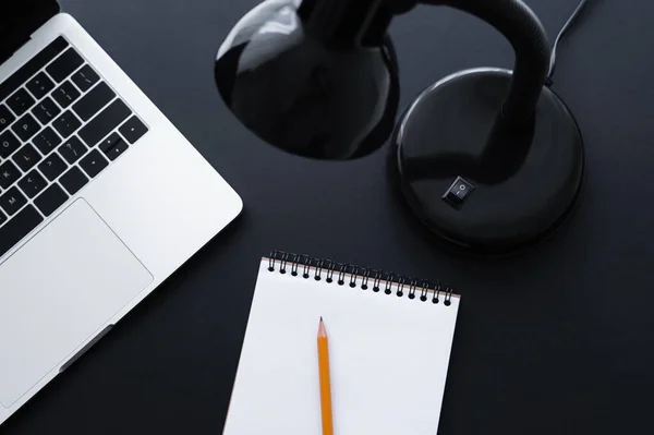Верхний вид лампы возле ноутбука и ноутбука с карандашом на черном — стоковое фото