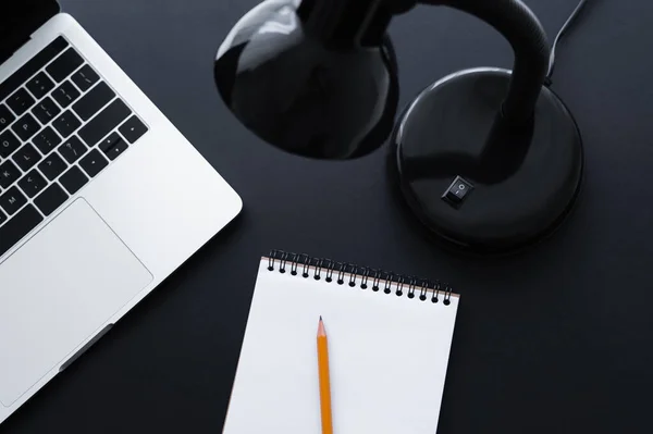 Top view of lamp near laptop and notebook with pencil on black — стоковое фото