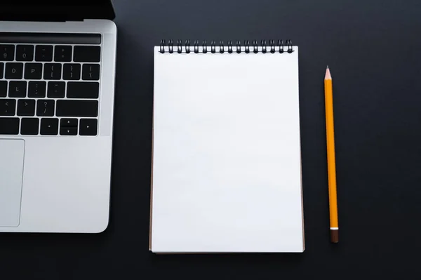 Vue du dessus de l'ordinateur portable près du cahier et du crayon sur noir — Photo de stock