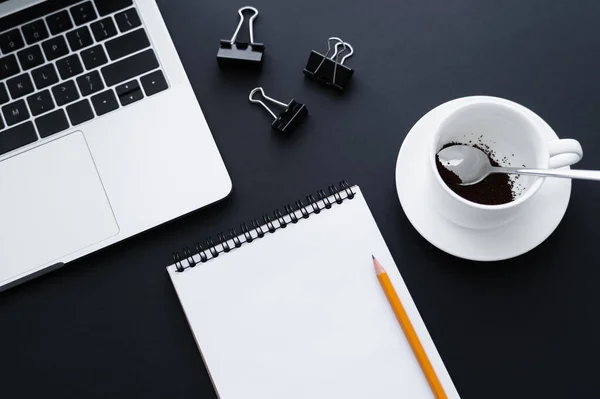 Top view of ground coffee in cup near fold back clips, notebook and laptop on black — Stockfoto