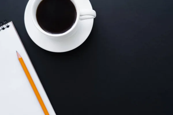 Top view of cup of coffee near notebook and pencil on black — Stockfoto