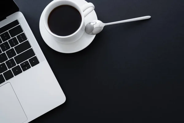 Top view of spoon on saucer with cup of coffee bear laptop on black — Photo de stock