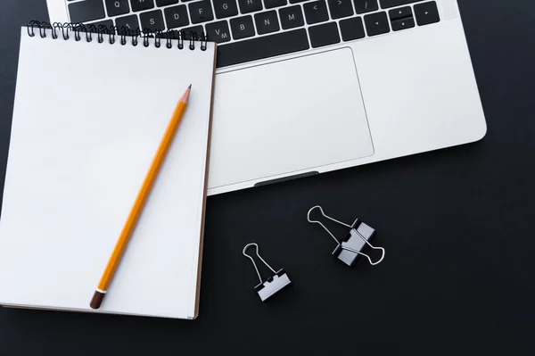 Top view of fold back clips near pencil on notebook and laptop on black — стоковое фото