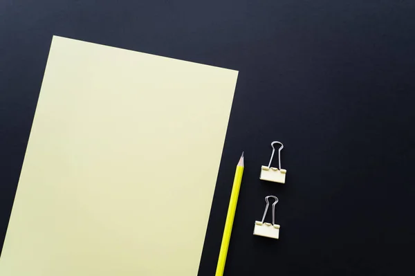 Top view of blank paper near pencil and fold back clips on black — Foto stock