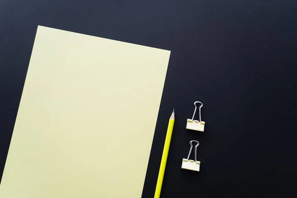 Top view of blank paper near pencil and fold back clips on black — Fotografia de Stock