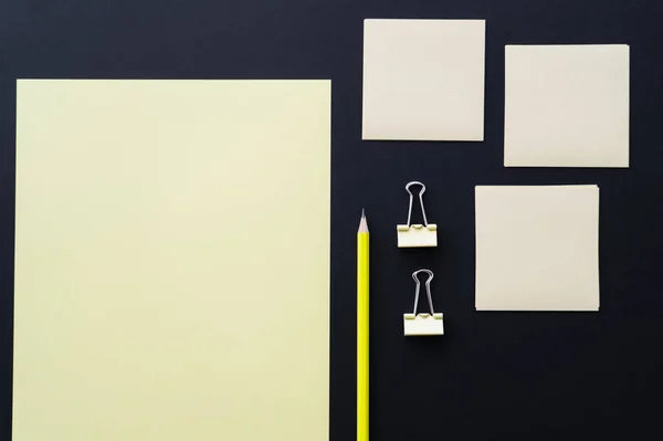 Top view of blank paper near sticky notes, pencil and fold back clips on black — Stock Photo