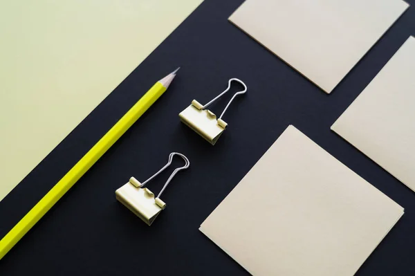 Flat lay of blank paper near sticky notes, pencil and fold back clips on black - foto de stock