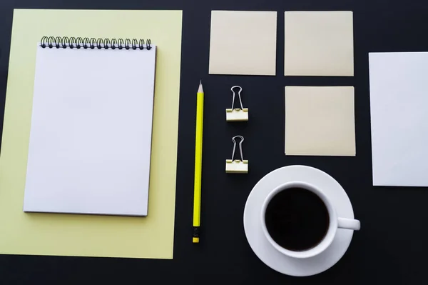 Flat lay of cup with coffee near sticky notes, pencil and notebook on black — Photo de stock