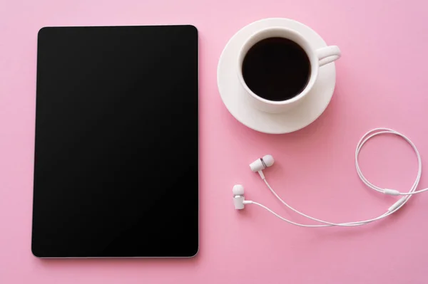 Top view of digital tablet with blank screen near cup of coffee and wired earphones on pink — стоковое фото