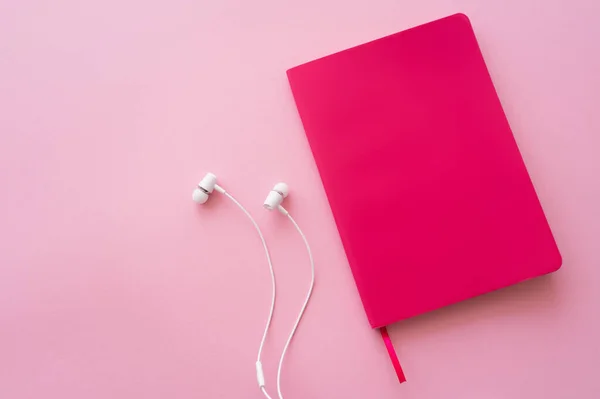 Top view of earphones near bright notebook on pink — Stock Photo