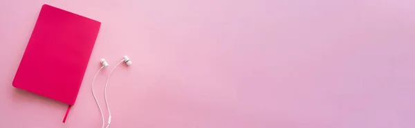 Vista superior de fones de ouvido perto de caderno brilhante em rosa, bandeira — Fotografia de Stock