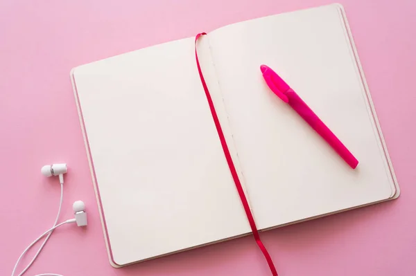 Вид зверху на відкритий ноутбук і ручку біля дротових навушників на рожевому — стокове фото