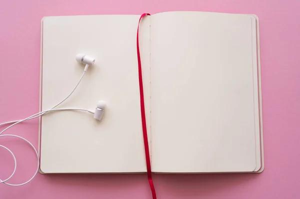 Top view of open notebook and wired earphones on pink — Stock Photo