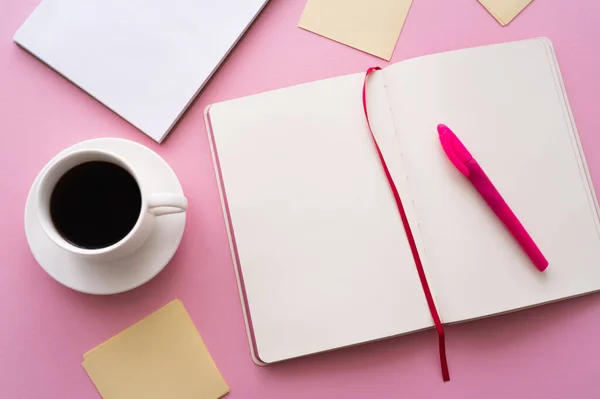 Vista superior da caneta no caderno aberto perto da xícara de café e notas de papel no rosa — Fotografia de Stock