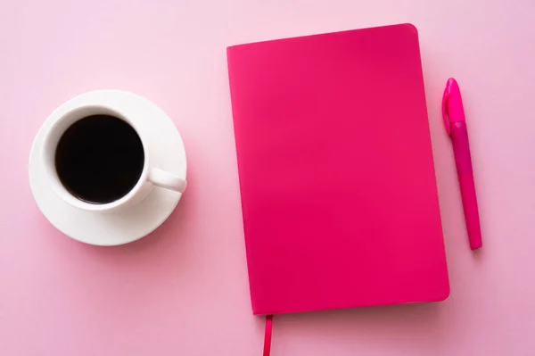 Top view of pen near bright notebook and cup of coffee on pink — стоковое фото