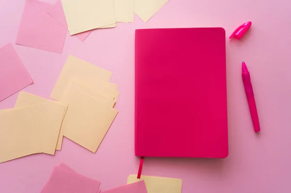 Vista superior de la pluma cerca de cuaderno brillante y notas de papel en rosa - foto de stock