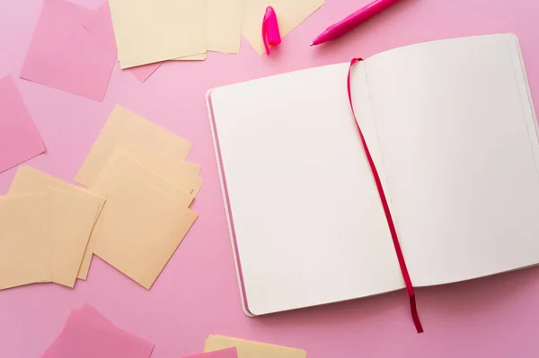 Vista superior de la pluma cerca de cuaderno abierto y notas de papel en rosa - foto de stock
