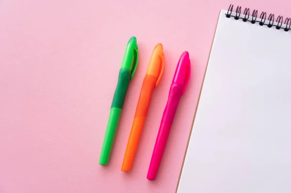 Draufsicht auf bunte und helle Stifte in der Nähe leeres Notizbuch auf rosa — Stockfoto