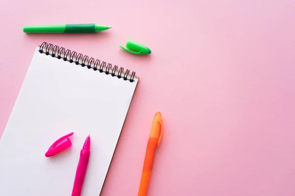 Вид зверху барвисті ручки біля порожнього ноутбука на рожевому — стокове фото
