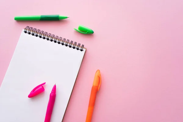 Top view of colorful pens near blank notebook on pink — стоковое фото