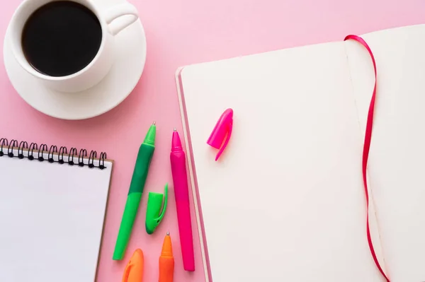 Vista superior de plumas de colores cerca de cuadernos en blanco y una taza de café en rosa - foto de stock