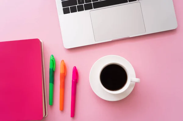 Vista superior do laptop perto de notebook, canetas e xícara de café em rosa — Fotografia de Stock