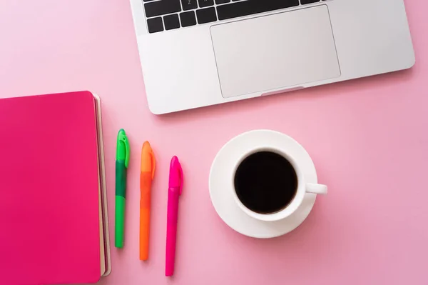 Vista superior de la computadora portátil cerca del portátil, bolígrafos y taza de café en rosa - foto de stock