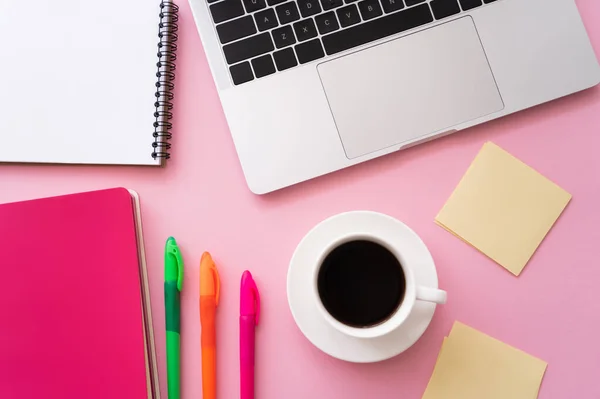 Vista superior de la computadora portátil cerca de papelería y taza de café en rosa - foto de stock