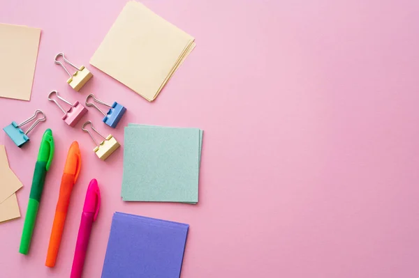 Vue du haut des pinces arrière près des notes en papier vierges colorées et des stylos sur rose — Photo de stock