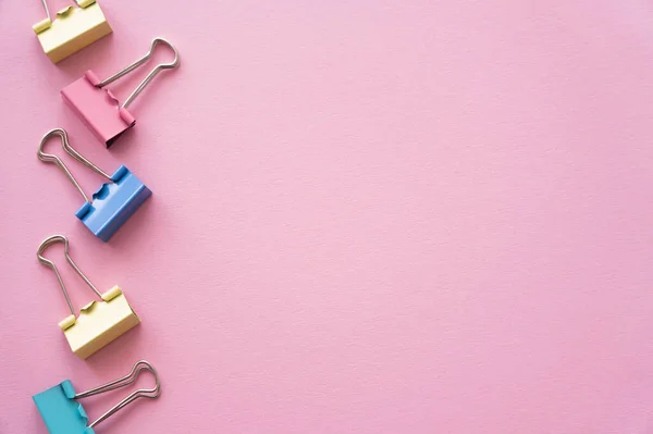 Flat lay of colorful pastel fold back clips on pink — стоковое фото